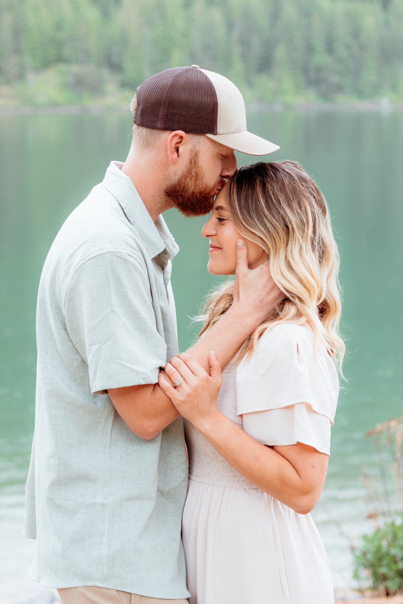 Couple embracing beside a green North Idaho lake during an engagement photo session
