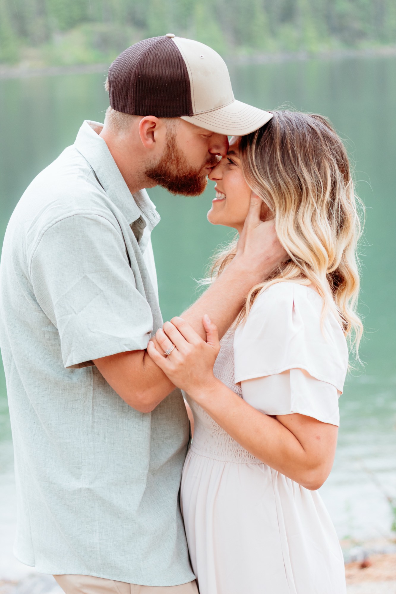 Engagement photos nose to nose beside a green North Idaho lake