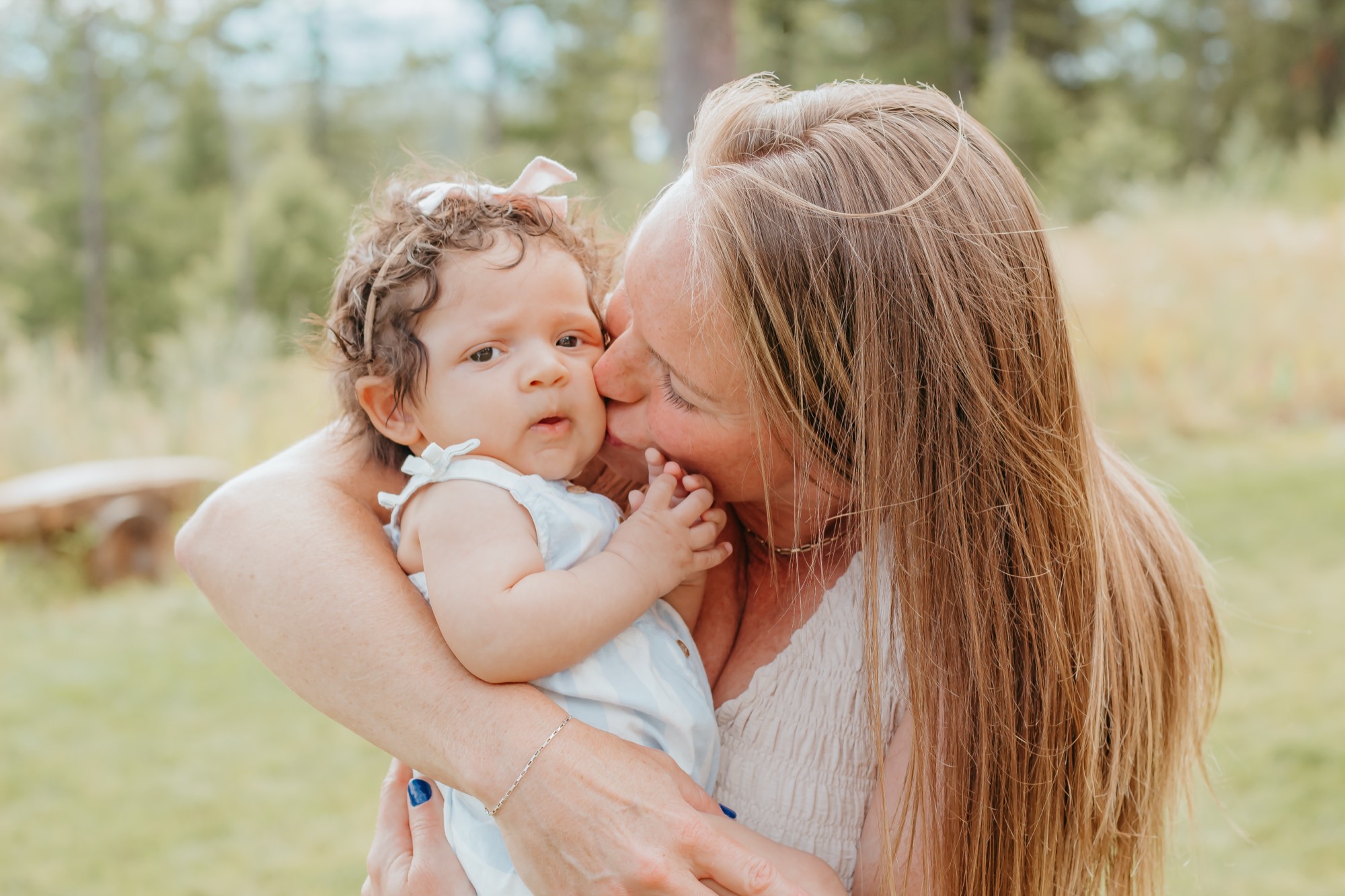 Mom kissing her baby daughter's cheek in a sunlit North Idaho meadow during a motherhood photo session