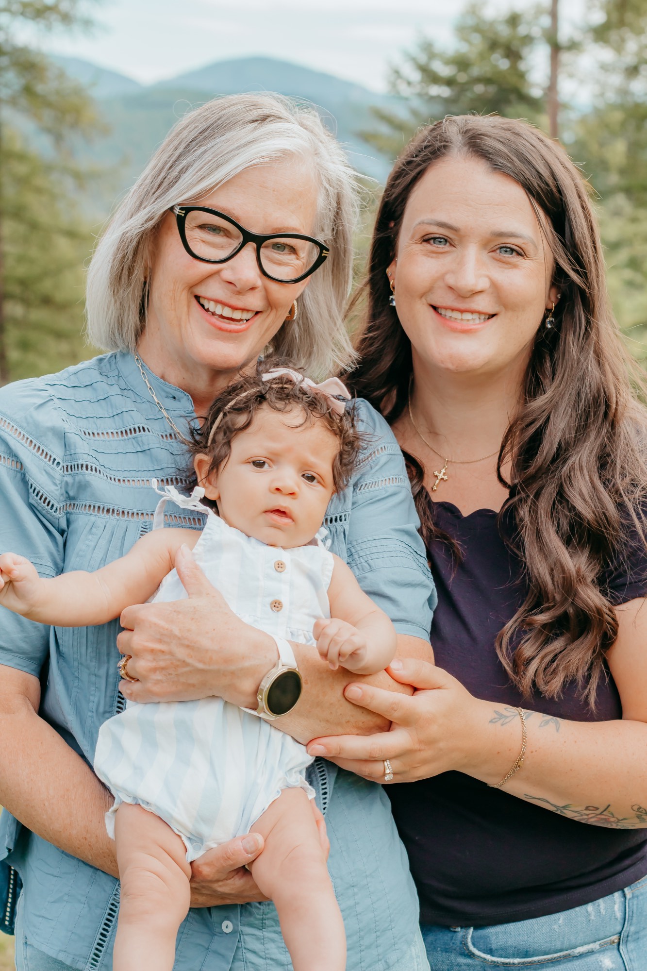 Three generations of women, grandmother mother and baby, facing the camera with North Idaho mountains behind them